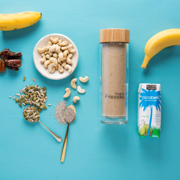 Glass fressko flask with smoothie inside surrounded by banana nuts seeds and dates