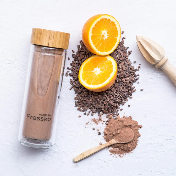 Glass fressko flask filled with jaffa smoothie surrounded by orange and cacao nibs