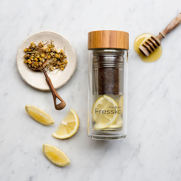 Lemon and honey chamomile tea in glass flask surrounded by lemon honey and chamomile